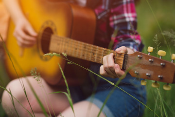 Close up shot of young girl playing guitar. Woman holding chords while playing guitar sitting on...