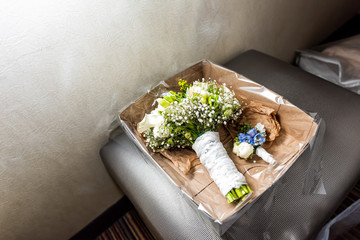 Wedding bouquet and boutonniere corsage in cardboard box in evening dark room, many flowers, green...