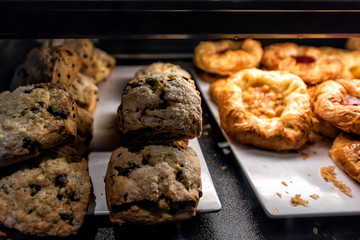 Closeup of many yellow dessert berry fruit baked danish pastries, blueberry sugar scones muffins on shelf tray retail display desserts in bakery shop cafe store dark counter