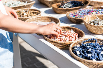 Closeup of young woman shopping for colorful stone beach bracelets touching hand in outdoor market shop store in European, Greece, Italy, Mediterranean town, village in summer