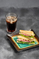 Sandwich with ham and cheese from white bread. Sliced bread is toasted. Near the glass with a carbonated drink. Gray background. Close-up. Vertical orientation of the frame.