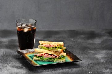 Sandwich with ham and cheese from white bread. Sliced bread is toasted. Near the glass with a carbonated drink. Gray background. Close-up. 