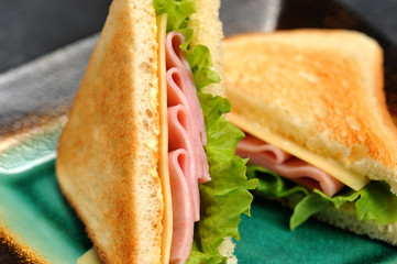 Sandwiches of a triangular shape on a plate. The filling of the sandwich consists of ham, cheese and leaves. Pieces of white bread fried. Close-up. Macro photography.