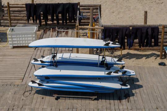 Rental station for surfboards, with swimsuits in the background, with white and blue surfboards on a rack


