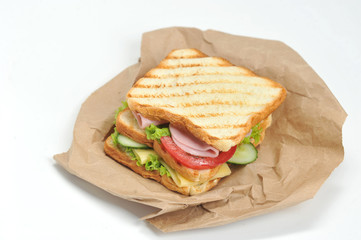 Sandwich with ham, cheese, lettuce, fresh cucumbers and tomatoes. Slices of white bread are grilled. The sandwich lies on the kraft paper. Close-up. White background.