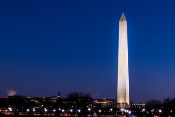 Tall high Washington Monument memorial in blue sky at evening night in winter, lawn, illuminated bright lights dark in December