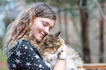 Happy young woman in dress holding maine coon cat outside, outdoors during summer in park with eyes...