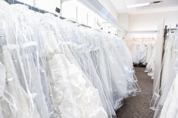 Many wedding dresses gowns in boutique discount store, white garments hanging on rack hangers row closeup with white lace, tulle, design
