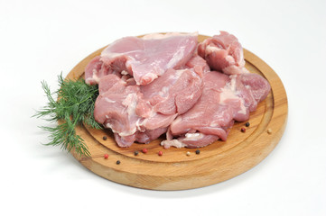 The fillet of the turkey hip is raw on a round wooden tray. Next to the meat is a branch of dill. White background. Close-up. 