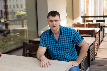Fototapeta premium young man. the man in the shirt in the cage. portrait of a man. a man at a table in a cafe in the open area.