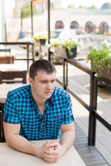 Fototapeta premium young man. the man in the shirt in the cage. portrait of a man. a man at a table in a cafe in the open area.