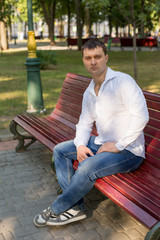 the guy is sitting on a bench in the Park. a man in a white shirt and jeans. young man. a man in a white shirt portrait of a man. business portrait. male portrai