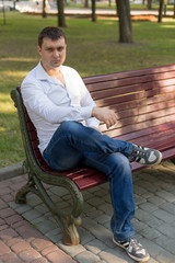 the guy is sitting on a bench in the Park. a man in a white shirt and jeans. young man. a man in a white shirt portrait of a man. business portrait. male portrai