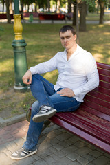 the guy is sitting on a bench in the Park. a man in a white shirt and jeans. young man. a man in a white shirt portrait of a man. business portrait. male portrai