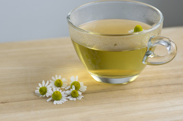 Matricaria chamomilla flowers and trasparent cup of tea on wooden table, fresh flowering herbal medicine