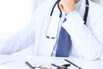 Unknown male doctor is sitting at the table and working in the hospital office. Closeup of stethoscope