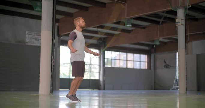 Young adult man doing skipping exercise with jumping rope during fitness sport workout .Grunge industrial urban training.4k slow motion video