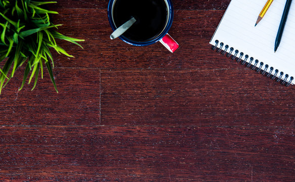 Top view of office wooden tabletop with green plant, enamel cup of coffee and bloc notes with pencil and pen. Copy space for product or texy. Business concept.