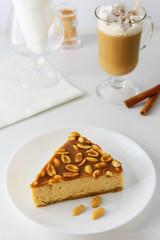Slice of caramel cake with peanuts and a cup of coffee with cream