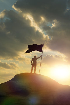 silhouette of a man on top of a mountain holding a flag of victory, against the sky and sunset. Concept business idea. achievements, success, career ladder, work