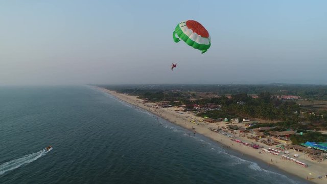 Towing a multicolored parachute behind a boat over the sea along the beach at sunset. Drone flied near the parachute. Aerial view.
