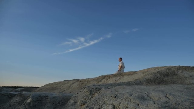 The strongman sits on his knees on the top of the hill and meditates