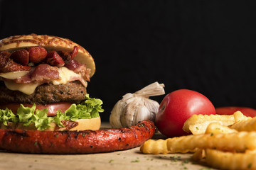 Hamburguesas y papas a la francesa en mesa de madera con sus ingredientes frescos como el tomate, lechuga, salchicha y cebolla