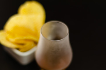 glass of whiskey with ice cubes and salty snacks on a black background