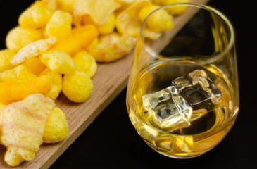 glass of whiskey with ice cubes and salty snacks on a black background