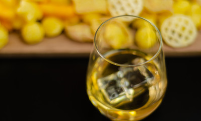 glass of whiskey with ice cubes and salty snacks on a black background