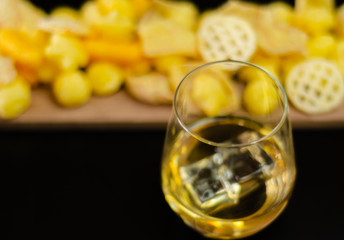 glass of whiskey with ice cubes and salty snacks on a black background