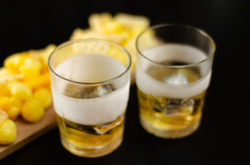 glass of whiskey with ice cubes and salty snacks on a black background