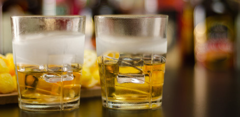 glass of whiskey with ice cubes and salty snacks on the background of bottles and bar