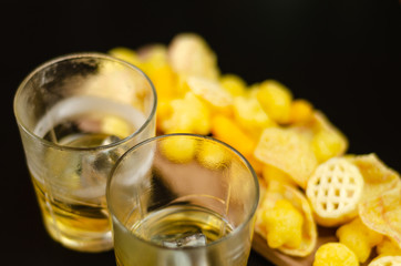 glass of whiskey with ice cubes and salty snacks on a black background