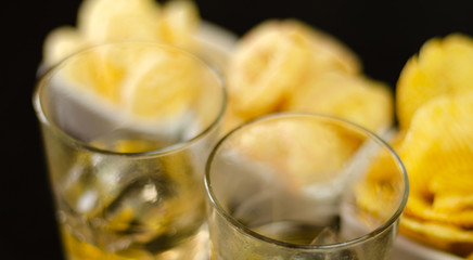 glass of whiskey with ice cubes and salty snacks on a black background