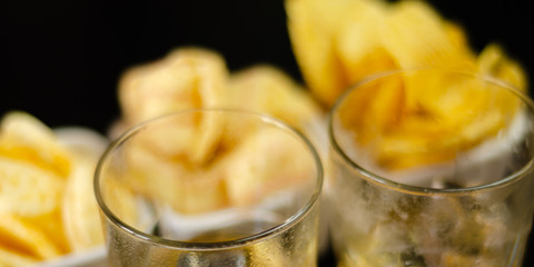 glass of whiskey with ice cubes and salty snacks on a black background