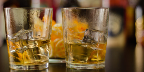 glass of whiskey with ice cubes and salty snacks on the background of bottles and bar