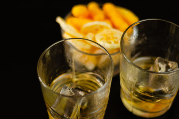 glass of whiskey with ice cubes and salty snacks on a black background