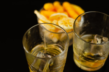 glass of whiskey with ice cubes and salty snacks on a black background