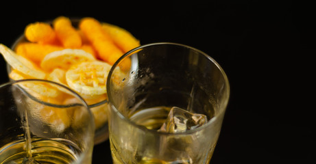 glass of whiskey with ice cubes and salty snacks on a black background