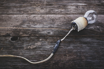 Concept - neglect of fire safety. Retro incandescent light bulb with damaged wires, on wooden...