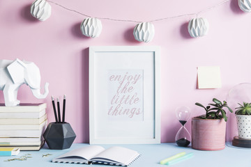 Stylish and modern desk with mock up photo frame, elephant figures, books, hanging cotton lamps and plants. Pink backgrounds wall. Lovely and design space.