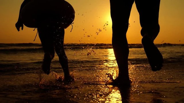Silhouette of the father and his little daughter are running happily into the sea at sunset. Splashes fly into their faces. Happy family with a child on vacation at the beach.