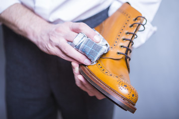 Closeup of hands of Professional Male Shoe Cleaner Using Cloth For Tan Derby Boots. Working in...