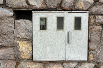 Electric meter box mounted on stone wall with one out of three meters inside and working