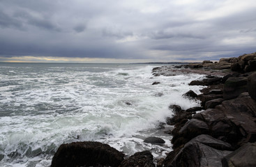 Obraz premium Small waves crash against rocky shore under dramatic storm clouds