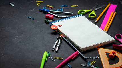 School supplies for school: notepad, pencils, pink ruler, compasses scattered on a gray table. Top view.