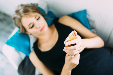 Beautiful young pregnant woman lying on sofa at home and using smartphone .