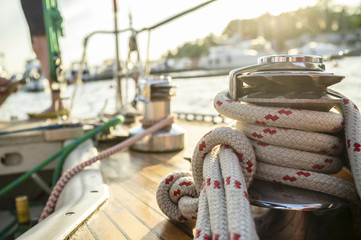 Sheet winch on the wooden deck of the yacht on a blurred background of the pier with boats, the sea...