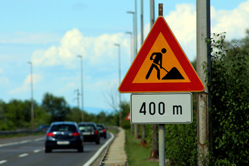 Road work ahead for 400 meters road sign near the road with multiple cars in background